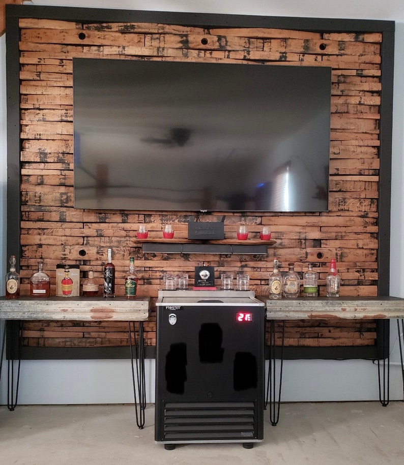 K&ouml;nnte beinhalten: Ein schwarzer K&uuml;hlschrank mit einem digitalen Temperaturdisplay, das auf 21 Grad Fahrenheit eingestellt ist. Der K&uuml;hlschrank steht auf einem Holztisch mit einem schwarzen Metallrahmen. Auf dem Tisch stehen Flaschen mit Spirituosen und Gl&auml;ser. Der K&uuml;hlschrank steht vor einer Wand aus wiederverwendeten Holzbrettern.