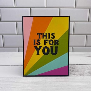 May include: A rectangular greeting card featuring a sunburst pattern of pink, orange, yellow, green, teal, and purple segments. The text THIS IS FOR YOU is printed in bold black capital letters across the centre of the colourful card design.