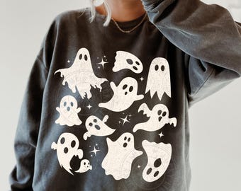 May include: Dark gray sweatshirt featuring a collection of white ghost illustrations. The ghosts vary in size and shape, with simple, expressive faces. The word "PEPPER" is printed at the bottom left corner of the image. The sweatshirt has a relaxed fit.