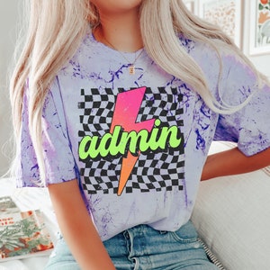 May include: A purple tie-dye t-shirt with a black and white chequered background and a pink and orange lightning bolt with the word "admin" in green letters.