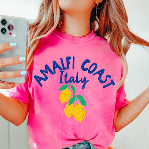 K&ouml;nnte beinhalten: Ein pinkfarbenes T-Shirt mit einer blauen Grafik, auf der "Amalfi Coast Italy" mit einem Zitronendesign steht.