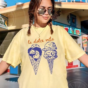 May include: A yellow t-shirt with a graphic of two ice cream cones and the text "la dolce vita" printed on the front.