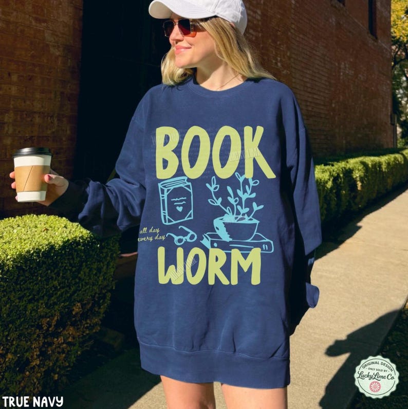 May include: Navy blue sweatshirt with the words "BOOK WORM" in lime green and light blue. The design includes a book, glasses, and a potted plant. The text "all day every day" is also included.