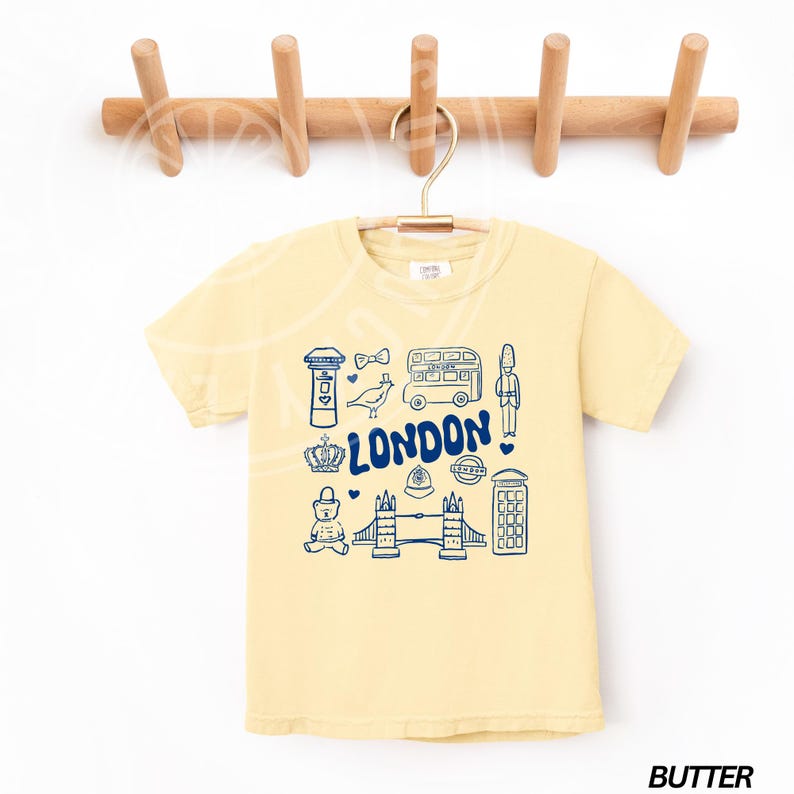 May include: A yellow t-shirt featuring a blue graphic of London landmarks, including a double-decker bus, Big Ben, a red telephone box, and Tower Bridge. The text "LONDON" is printed in blue on the shirt.