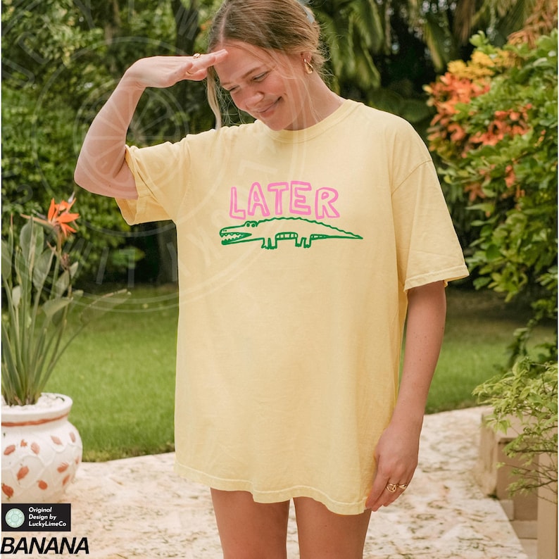 May include: A yellow t-shirt with a green alligator and the word "LATER" in pink letters. The shirt is oversized and has a relaxed fit.