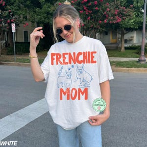 May include: White t-shirt with the words "FRENCHIE MOM" in orange block letters. The shirt features blue line drawings of two French Bulldogs and the text "It is better with french bulldogs."