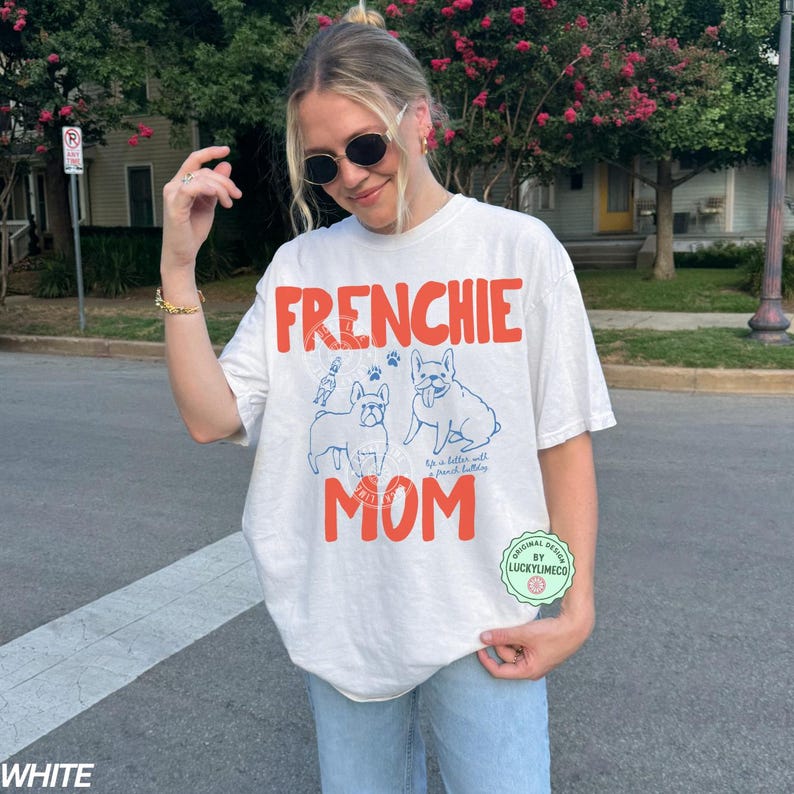 May include: White t-shirt with the words "FRENCHIE MOM" in orange block letters. The shirt features blue line drawings of two French Bulldogs and the text "It is better with french bulldogs."