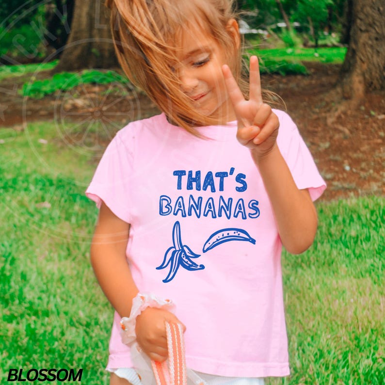 Op de afbeelding: Een roze T-shirt met een blauwe afbeelding van bananen en de tekst "That's Bananas".