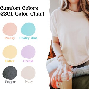 以下が含まれることがあります： 「Peachy」、「Chalky Mint」、「Butter」、「Orchid」、「Pepper」、「Ivory」とラベル付けされた6つの塗料見本があるカラーチャート。チャートのタイトルは「Comfort Colors 3023CL Color Chart」です。