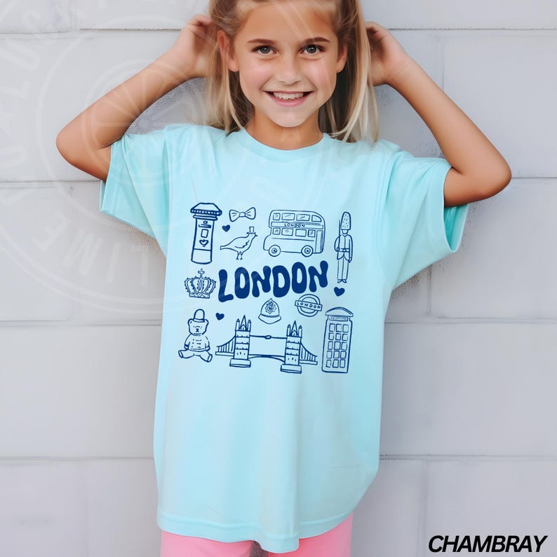 May include: A light blue t-shirt featuring a graphic design of London landmarks in blue. The landmarks include a double-decker bus, a red telephone box, Big Ben, and Tower Bridge. The text "LONDON" is written in a stylised font.
