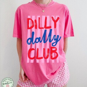 May include: A pink t-shirt with the words "DILLY dally CLUB" in red and blue, set against pink vertical stripes. The shirt is paired with pink and white checkered shorts. The design includes the text "CRUNCHBERRY" and a logo.