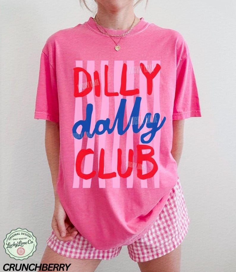 May include: A pink t-shirt with the words "DILLY dally CLUB" in red and blue, set against pink vertical stripes. The shirt is paired with pink and white checkered shorts. The design includes the text "CRUNCHBERRY" and a logo.