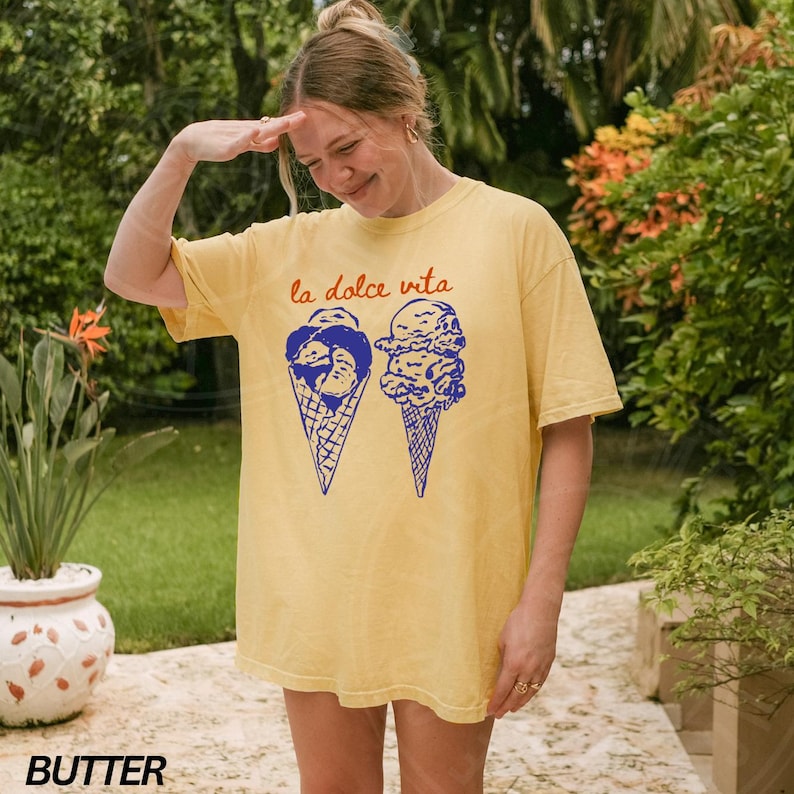 May include: A yellow t-shirt featuring a graphic of two ice cream cones and the text "la dolce vita" in blue and orange.