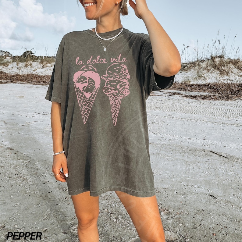 Op de afbeelding: Een oversized donkergroen t-shirt met een afbeelding van twee ijshoorns en de tekst "la dolce vita" in roze.