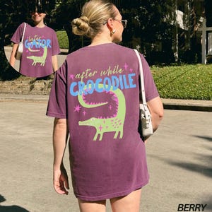 May include: Berry-colored t-shirt with a green crocodile graphic and the text "after while CROCODILE". The design includes pink stars and the text "later GATOR" on the front. The shirt is a casual style.
