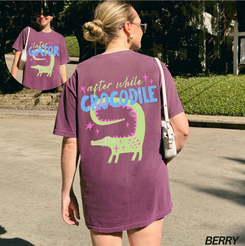 May include: Berry-colored t-shirt with a green crocodile graphic and the text "after while CROCODILE". The design includes pink stars and the text "later GATOR" on the front. The shirt is a casual style.
