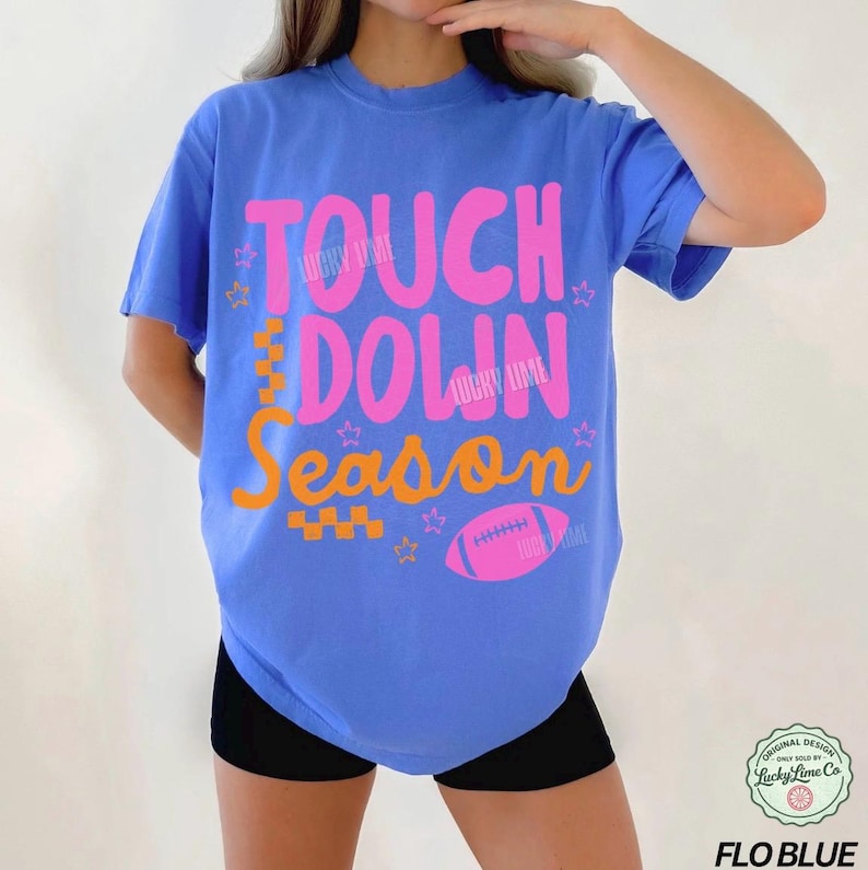 May include: A blue t-shirt with the words "TOUCH DOWN SEASON" in pink and orange, along with a pink football graphic. The shirt also has the text "LUCKY LIME" in pink. The shirt is a Flo Blue color.