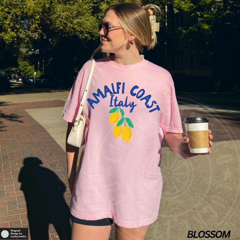 K&ouml;nnte beinhalten: Ein pinkfarbenes T-Shirt mit einer blauen Grafik, auf der "Amalfi Coast Italy" mit einem Zitronendesign steht.