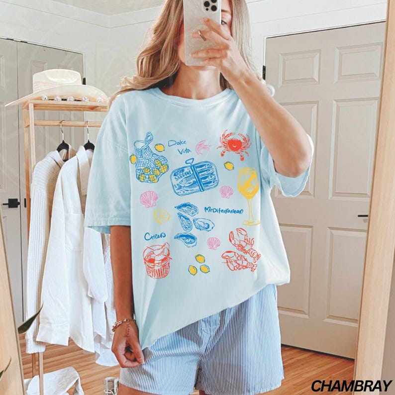 May include: A light blue t-shirt with a graphic print of various seafood and the text "Dolce Vita" and "Mediterranean".