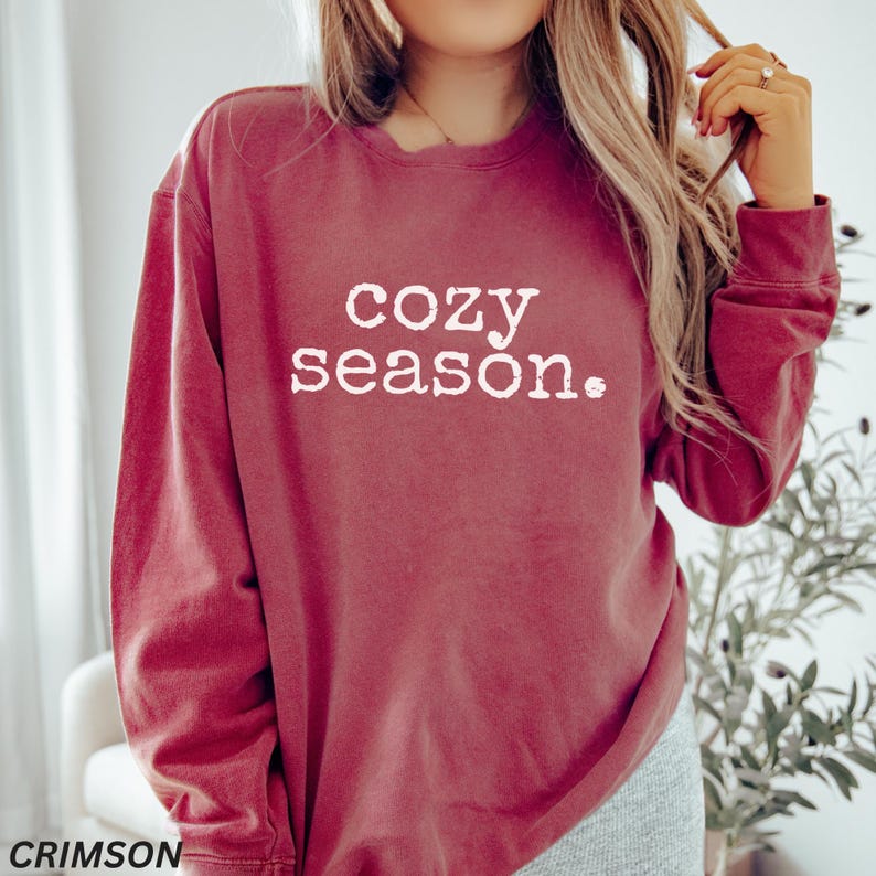 May include: A crimson red long-sleeved sweatshirt with the text "cozy season." printed in white.