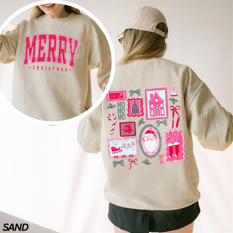 May include: Sand-colored sweatshirt with the word "MERRY" in pink, arched across the chest, and "CHRISTMAS" below. The back features a collage of pink and gray Christmas-themed illustrations, including Santa, gifts, and a house.