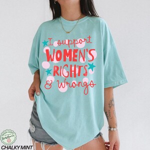 Peut inclure: T-shirt bleu clair avec l'inscription "I support WOMEN'S RIGHTS & Wrongs" en rouge et rose. Le t-shirt a une coupe ample et des manches courtes. Le texte est orn&eacute; de pois roses et d'&eacute;toiles bleues.