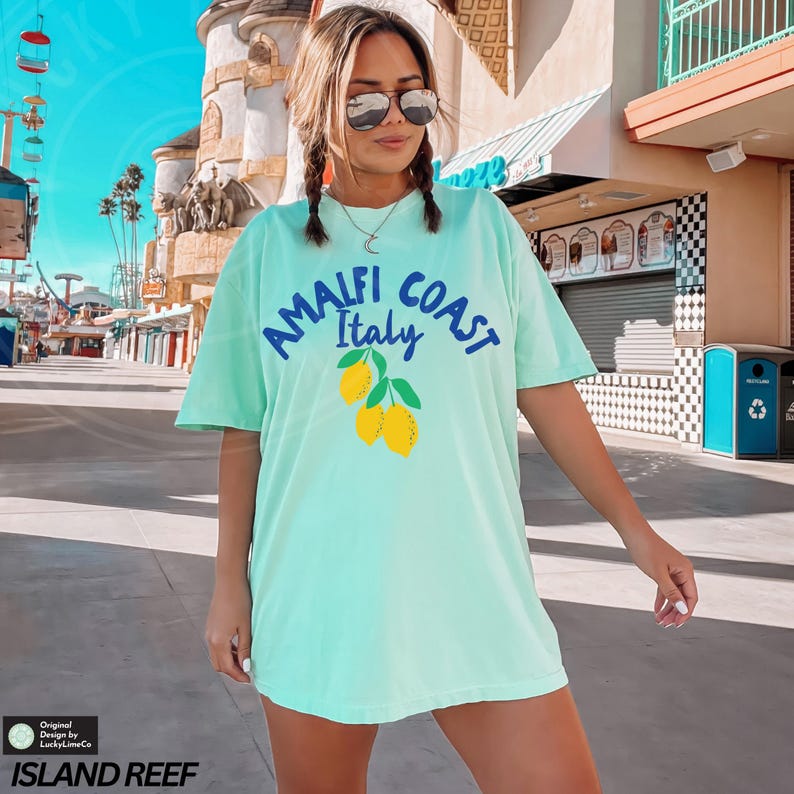 K&ouml;nnte beinhalten: Ein hellblaues T-Shirt mit einem grafischen Aufdruck von Zitronen und dem Text "Amalfi Coast Italy".