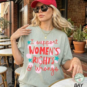 Peut inclure: T-shirt vert sauge avec l'inscription "I support WOMEN'S RIGHTS & Wrongs" en rouge et rose. Le motif comprend des pois roses et des &eacute;toiles bleues. Le t-shirt a une coupe d&eacute;contract&eacute;e et des manches courtes.