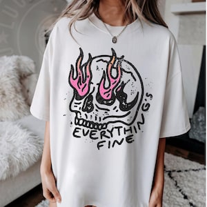 May include: White oversized t-shirt with a graphic print of a skull with flames for eyes and the text "Everything Fine".