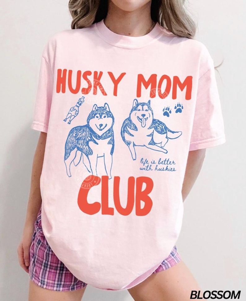 K&ouml;nnte beinhalten: Hellrosa T-Shirt mit dem Schriftzug "HUSKY MOM CLUB" in roten Buchstaben. Das Design zeigt blaue Illustrationen von zwei Huskys, Pfotenabdr&uuml;cken und den Satz "life is better with huskies".