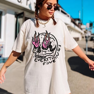May include: A white oversized t-shirt with a black and pink skull graphic. The skull has flames coming out of its eyes and the text "EVERYTHING'S FINE" is written below the skull.