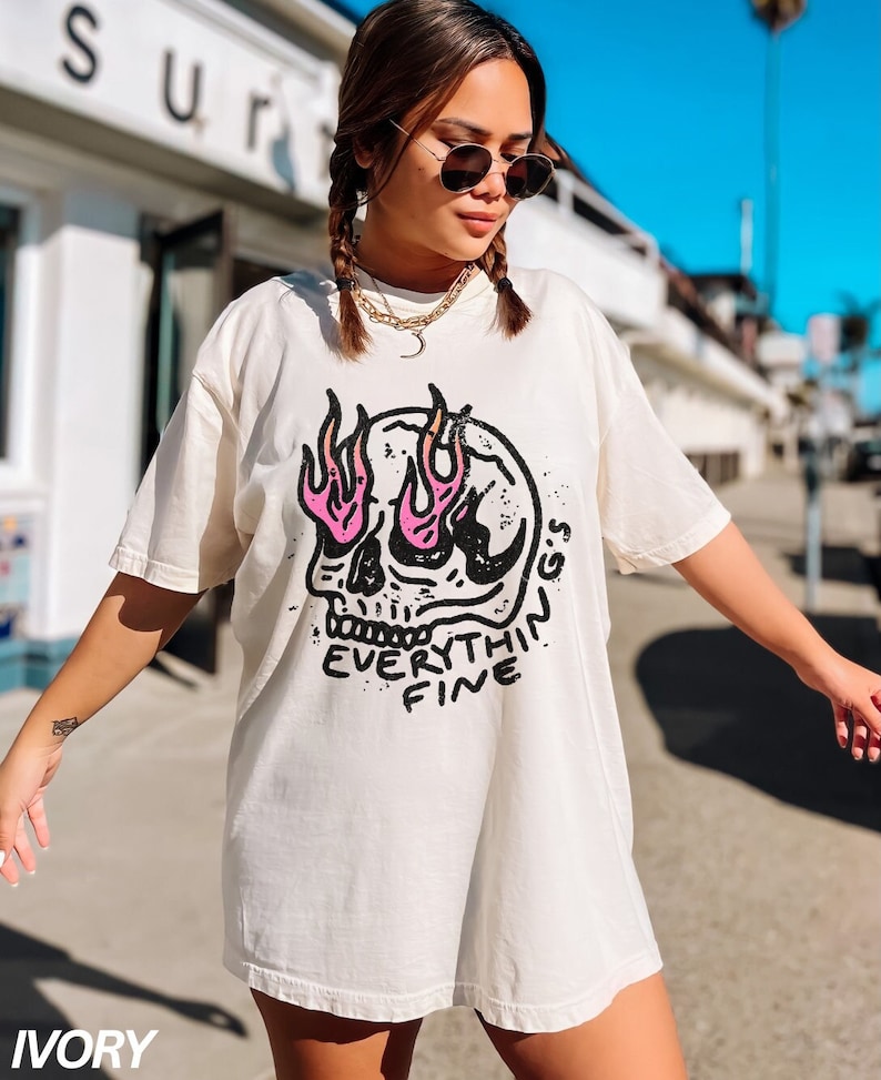 May include: A white oversized t-shirt with a black and pink skull graphic. The skull has flames coming out of its eyes and the text "EVERYTHING'S FINE" is written below the skull.