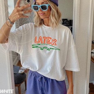 May include: White oversized t-shirt with a green and orange alligator graphic and the word "LATER" printed on the front.