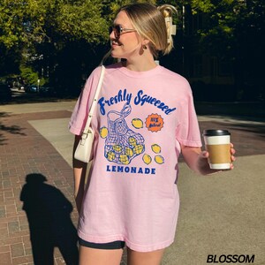 Puede incluir: Camiseta rosa con un gr&aacute;fico de una bolsa de malla llena de limones y el texto "Freshly Squeezed 100% Natural LEMONADE".