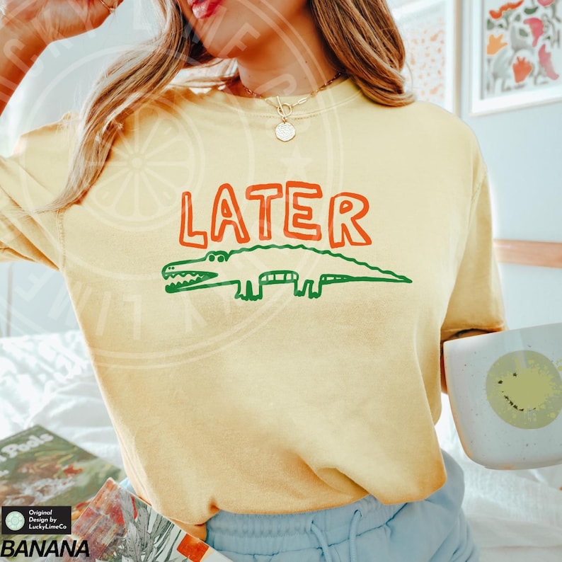 May include: A yellow t-shirt with the word "LATER" in red and green letters and a green and red alligator illustration.