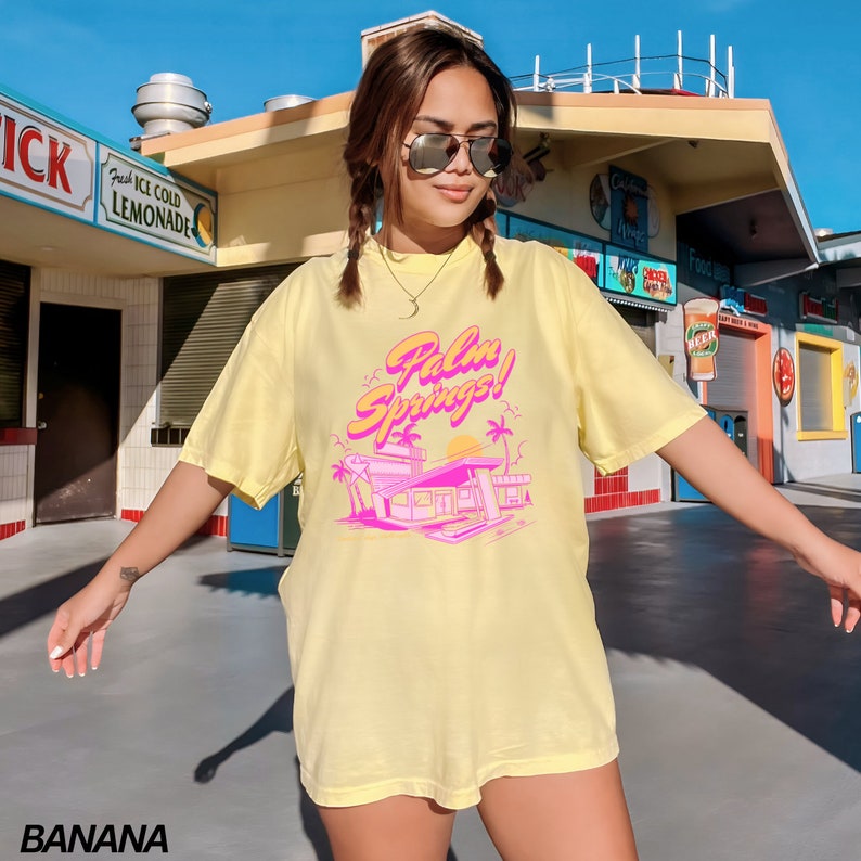 May include: A yellow t-shirt with a pink graphic of a building with palm trees and the text "Palm Springs!" printed on it.