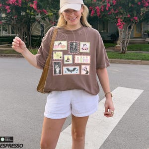 May include: A brown t-shirt with a collection of Halloween-themed postage stamp designs. The stamps feature pumpkins, skeletons, bats, and potion bottles. The shirt is paired with white shorts and a tan baseball cap.