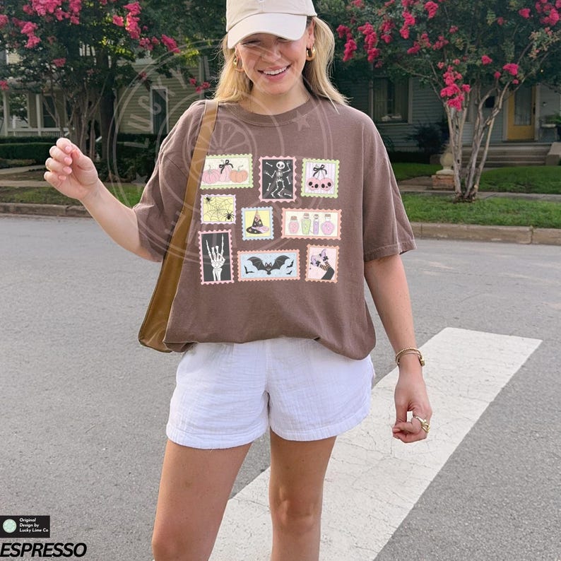 May include: A brown t-shirt with a collection of Halloween-themed postage stamp designs. The stamps feature pumpkins, skeletons, bats, and potion bottles. The shirt is paired with white shorts and a tan baseball cap.