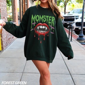 May include: Forest green sweatshirt with a graphic print of a dripping vampire mouth with fangs and the word "MOMSTER" in green letters.