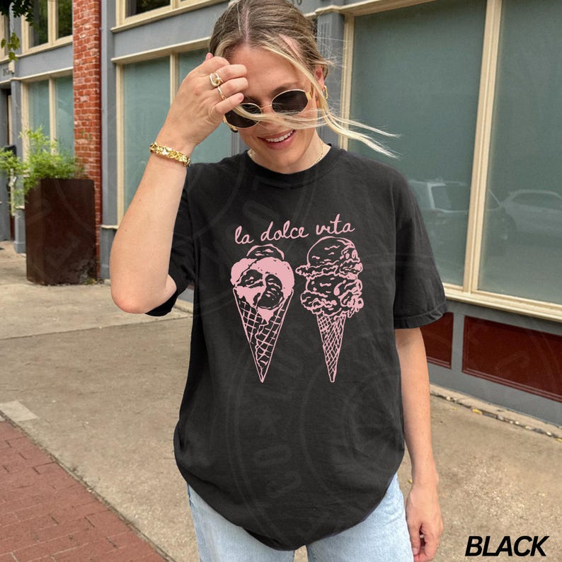 Op de afbeelding: Zwart T-shirt met een roze afbeelding van twee ijshoorns en de tekst "la dolce vita".