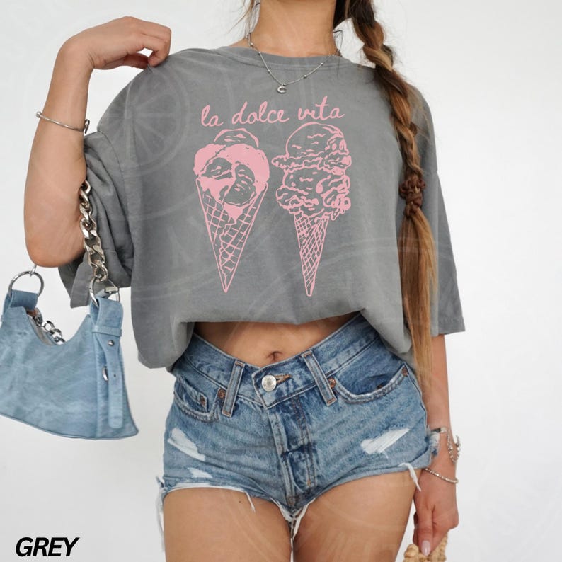Op de afbeelding: Een grijs gecropped t-shirt met de tekst "la dolce vita" en een roze afbeelding van twee ijshoorns.