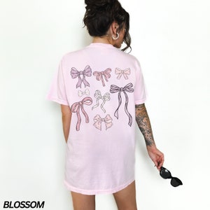 May include: A pink t-shirt with a graphic of multiple pink and purple bows on the back.