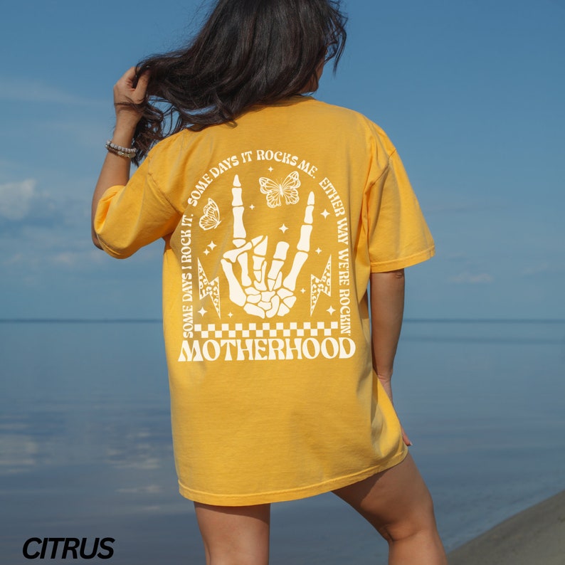 May include: A yellow t-shirt with a graphic on the back that says "SOME DAYS I ROCK IT. SOME DAYS IT ROCKS ME. EITHER WAY WE'RE ROCKIN' MOTHERHOOD." The graphic includes a skeleton hand, butterflies, and lightning bolts. The word "CITRUS" is at the bottom.