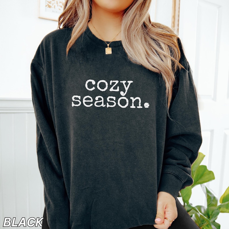 May include: Black long-sleeved sweatshirt with the text "cozy season." printed in white.
