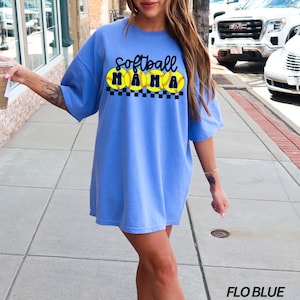Op de afbeelding: Een oversized lichtblauw t-shirt met de tekst "Softball Mama" en een afbeelding van vier gele softbal met zwarte naden.