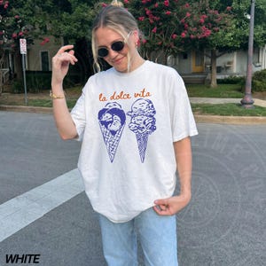 May include: White t-shirt featuring a graphic of two ice cream cones with the text "la dolce vita" in orange.