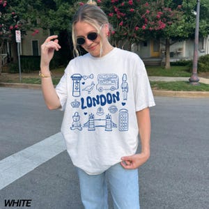 May include: White t-shirt with a blue graphic print of London landmarks, including a double-decker bus, a red telephone booth, a crown, and the words "LONDON".
