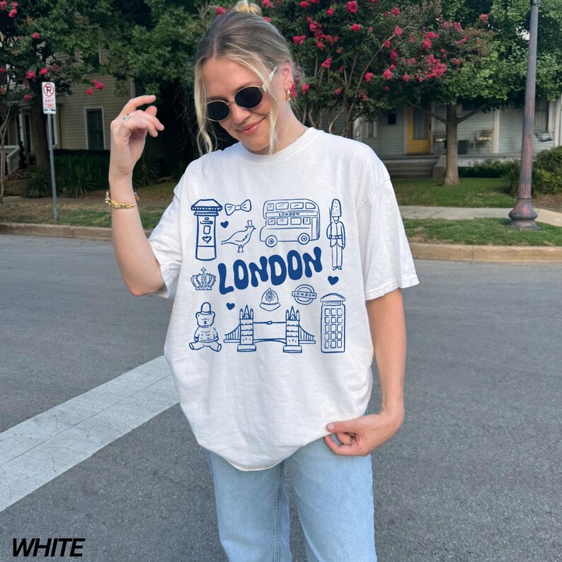 May include: White t-shirt with a blue graphic print of London landmarks, including a double-decker bus, a red telephone booth, a crown, and the words "LONDON".
