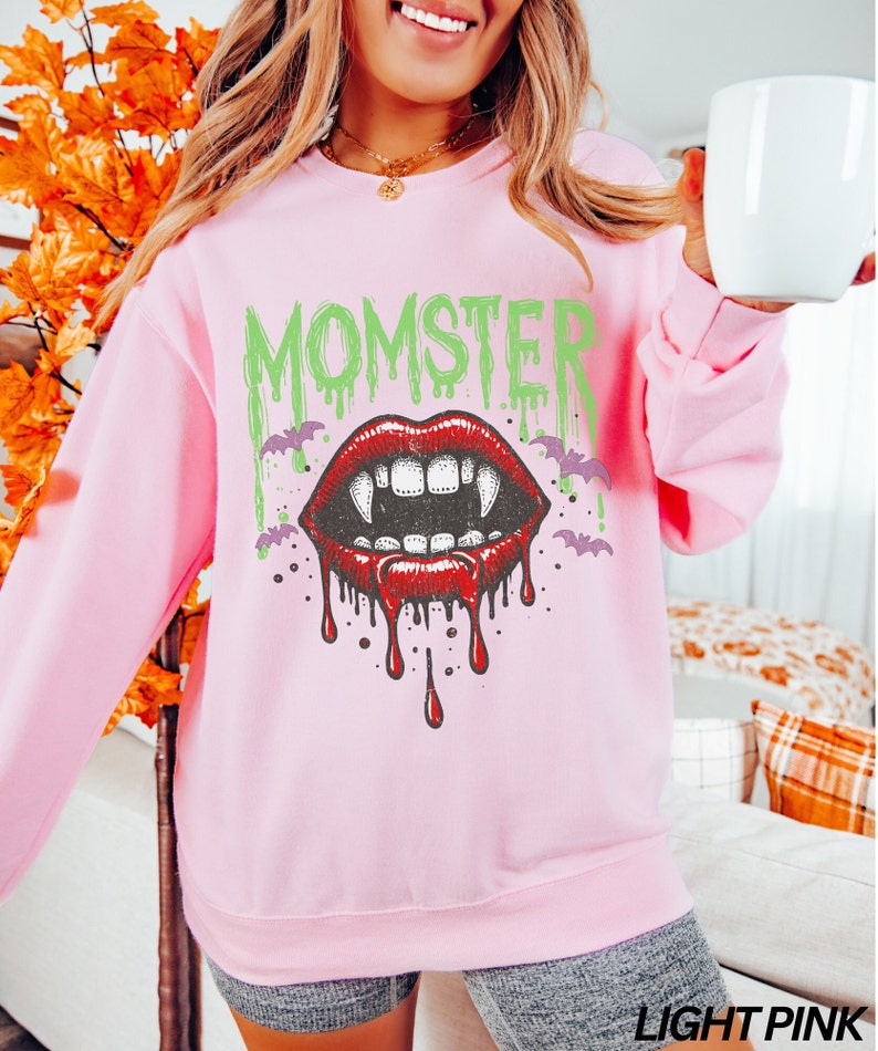 May include: A light pink sweatshirt with a graphic print of a dripping vampire mouth with fangs and the word "MOMSTER" in green letters.