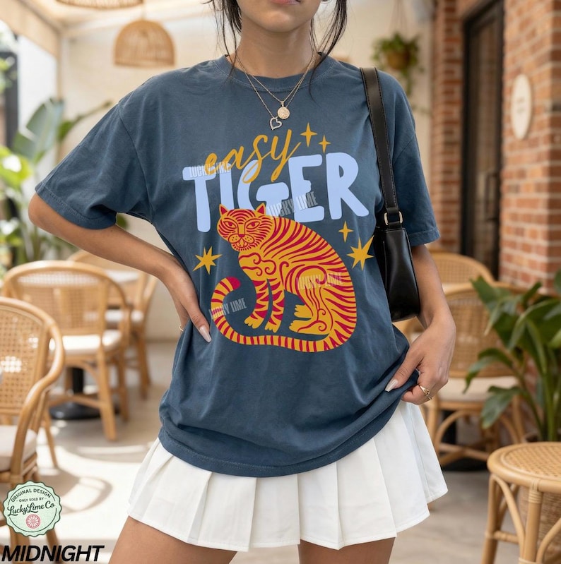 May include: Navy blue t-shirt with the text "easy TIGER" above a stylized orange and red tiger illustration. The design includes yellow star accents. The shirt is a relaxed fit.
